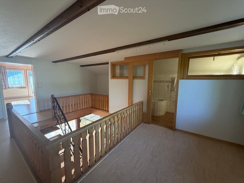 Spacious hallway with wooden staircase, open wooden doors leading to rooms, and a view of a tiled bathroom area.