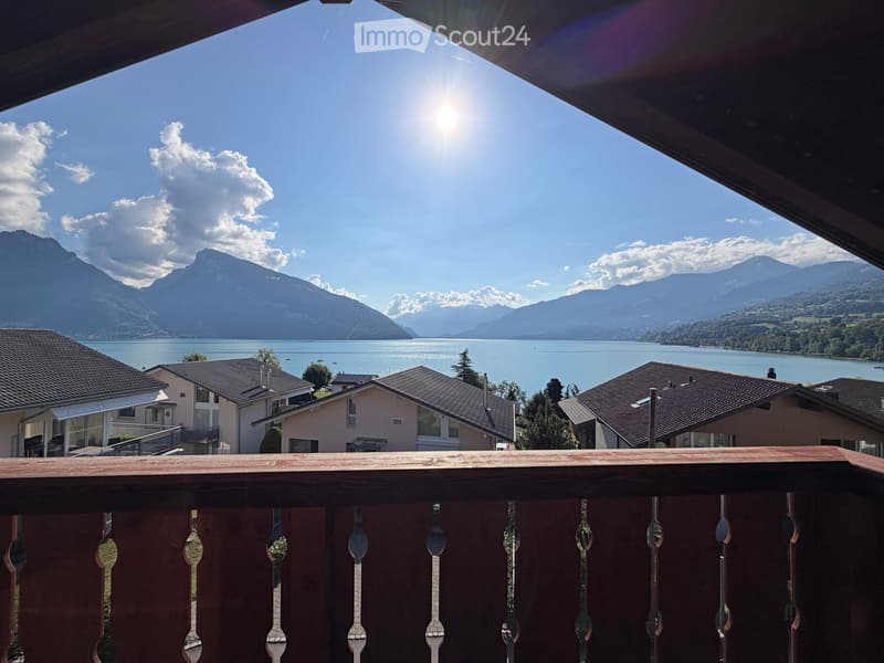 Balcony overlooking a scenic lake and mountain range, with neighboring houses visible in the foreground.