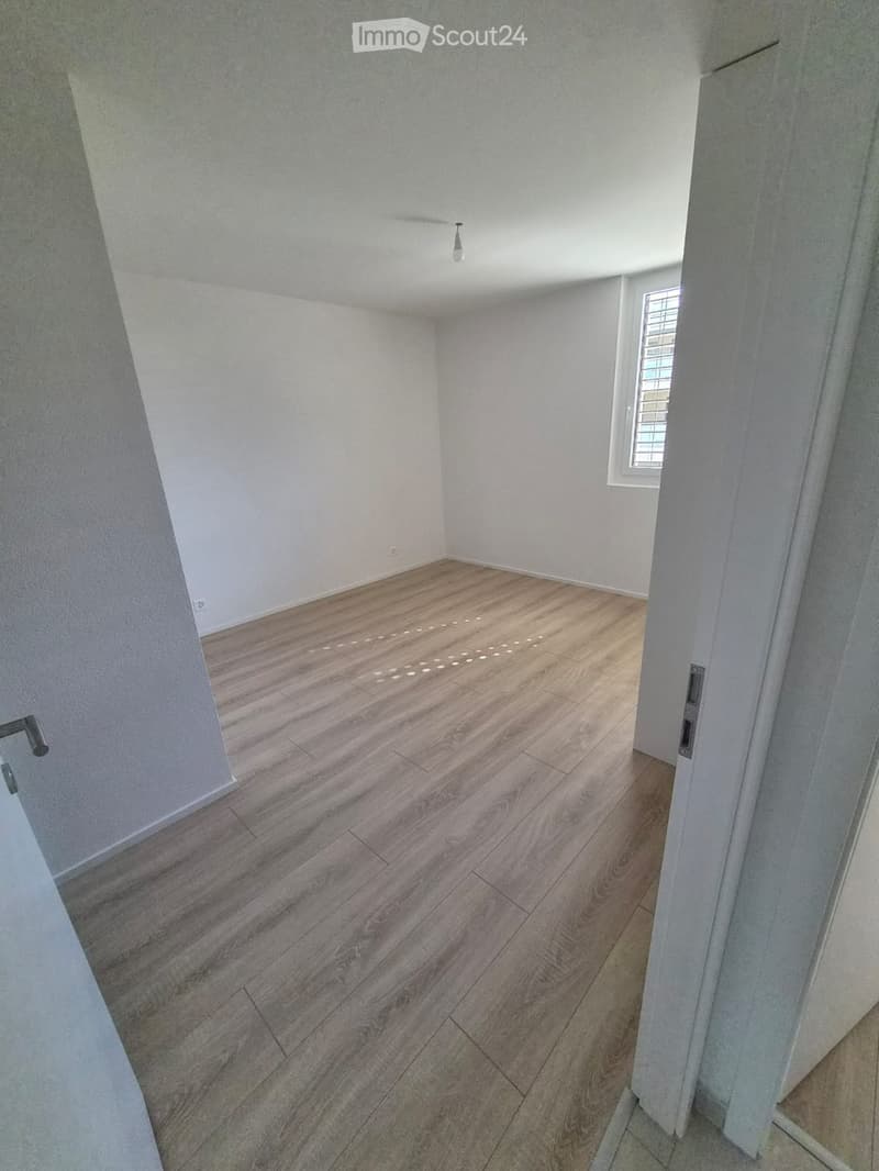 Empty room with wooden flooring, white walls, and a small window with bars. No furniture or equipment is present.