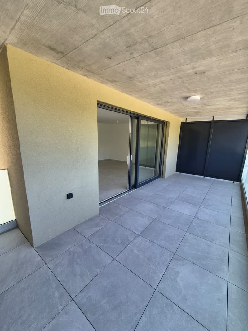 Modern balcony with tiled floor, sliding glass door leading to an adjacent room, and a dark privacy screen on one side.