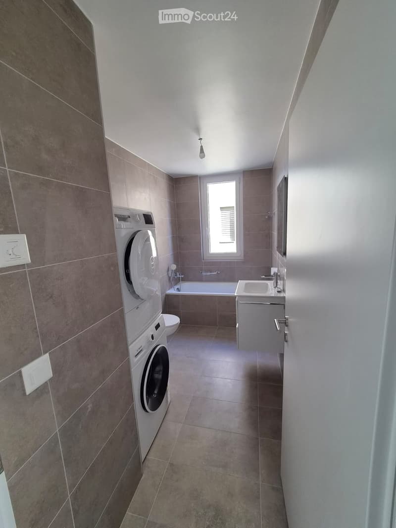 Modern bathroom with tiled walls, a washing machine, a sink, a bathtub, and a toilet.