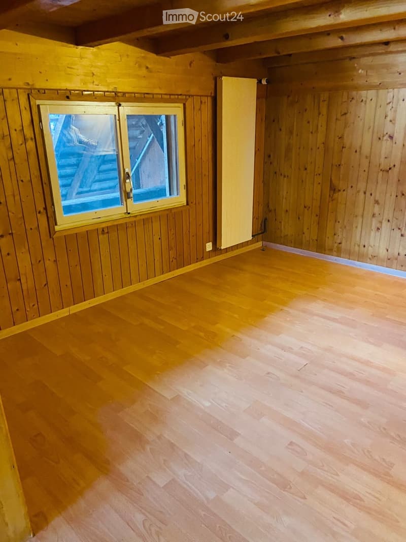 Empty room with wooden walls and floor, featuring a single window with a view of stairs.
