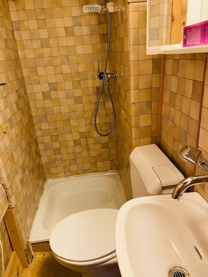Small bathroom with beige tiled walls, a bathtub, a toilet, a sink, and a showerhead with a hose.