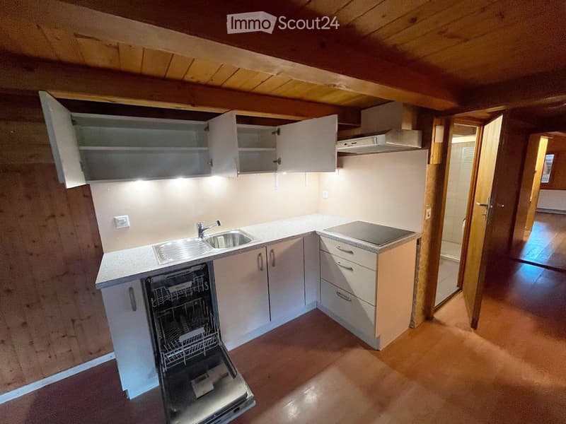 Modern kitchen with white cabinets, stainless steel sink, dishwasher, and countertop. Wooden ceiling beams and warm lighting.