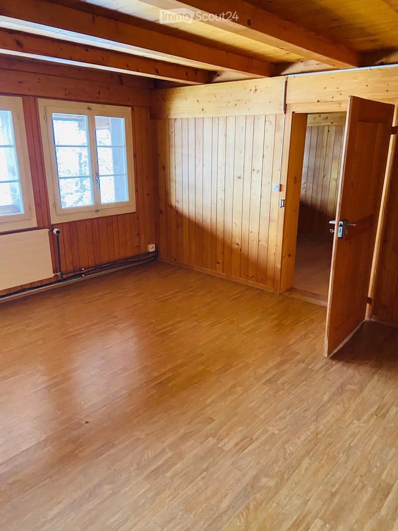 Empty room with wooden walls, wooden floor, and large windows. No furniture or equipment present.