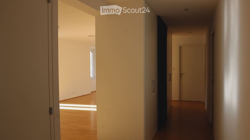 Empty hallway with wooden floors, white walls, and a door at the end.