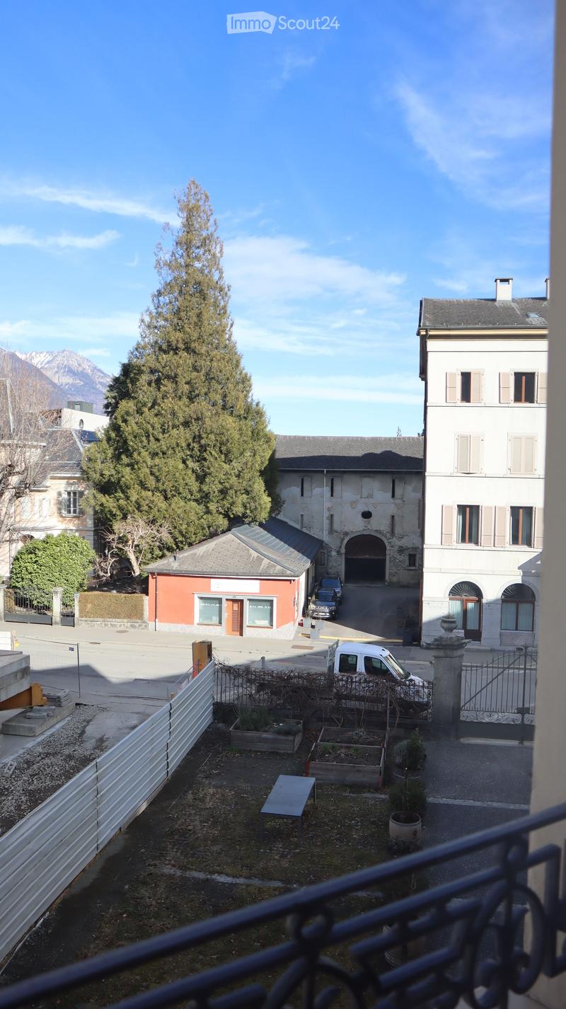 Aerial view of a building with a tree in front, a car parked in the street, and a mountain in the background.
