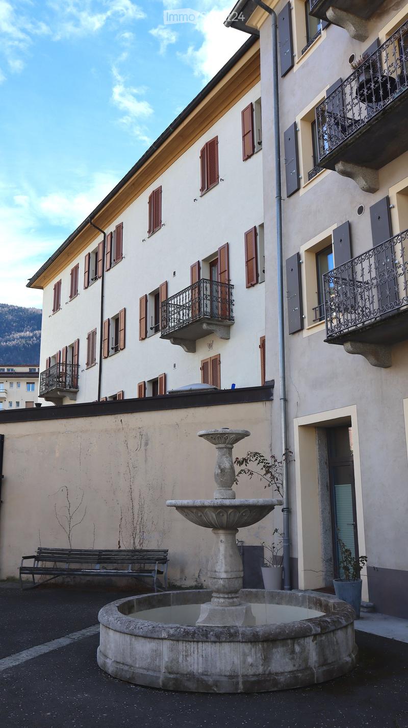 white building with brown shutters, balconies, fountain in front