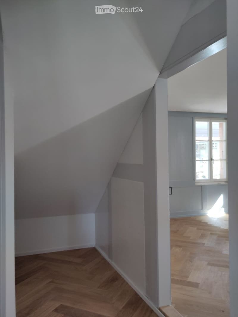 empty attic room, wooden floor, white walls, slanted ceiling, window