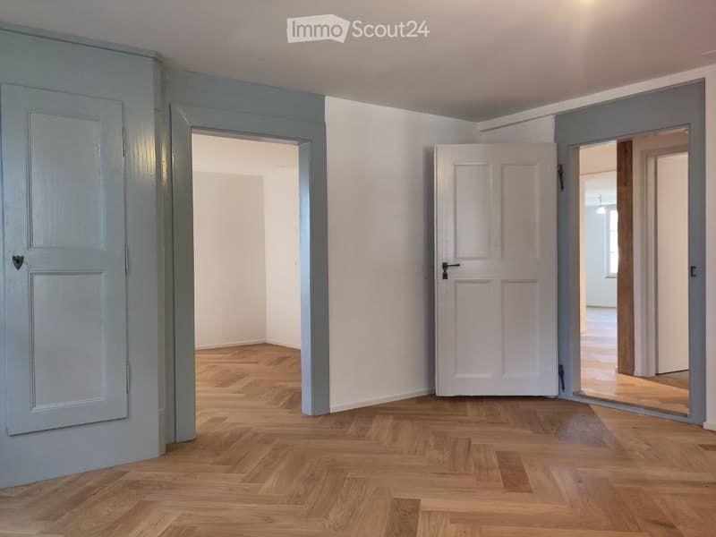 Empty room with wooden flooring, white walls, and two open doors leading to adjacent spaces.