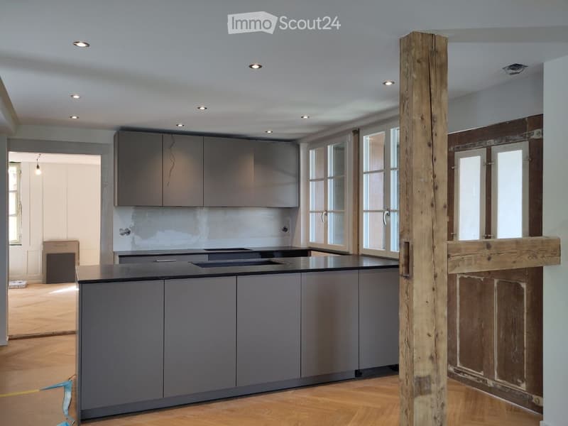 modern kitchen with island, gray cabinets, black countertops, wooden pillar, large windows