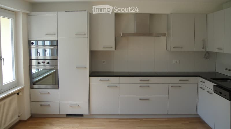 Modern kitchen with white cabinets, stainless steel oven, black countertop, and range hood.