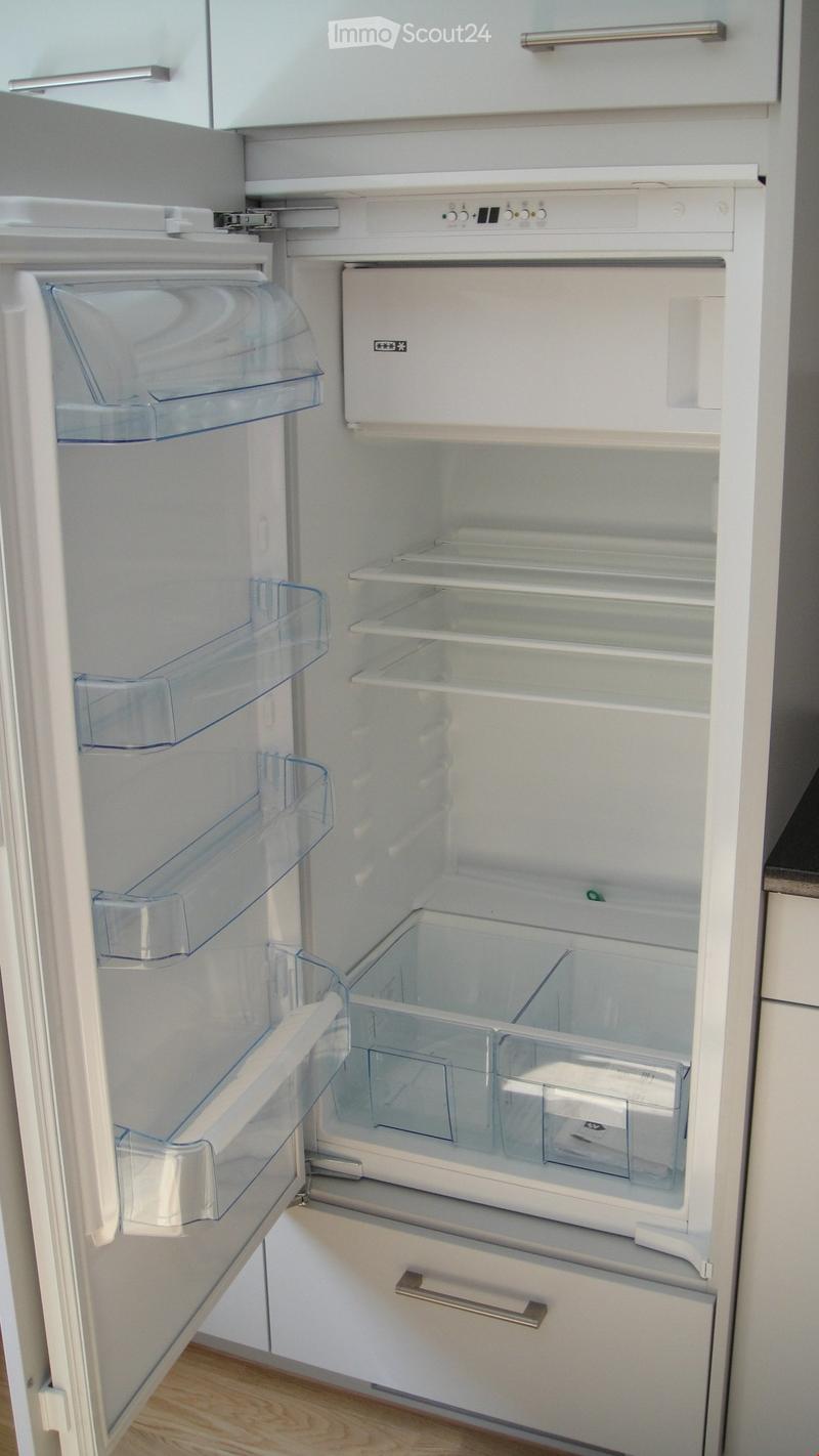 Open refrigerator with multiple shelves and compartments, including a freezer section with clear plastic bins.