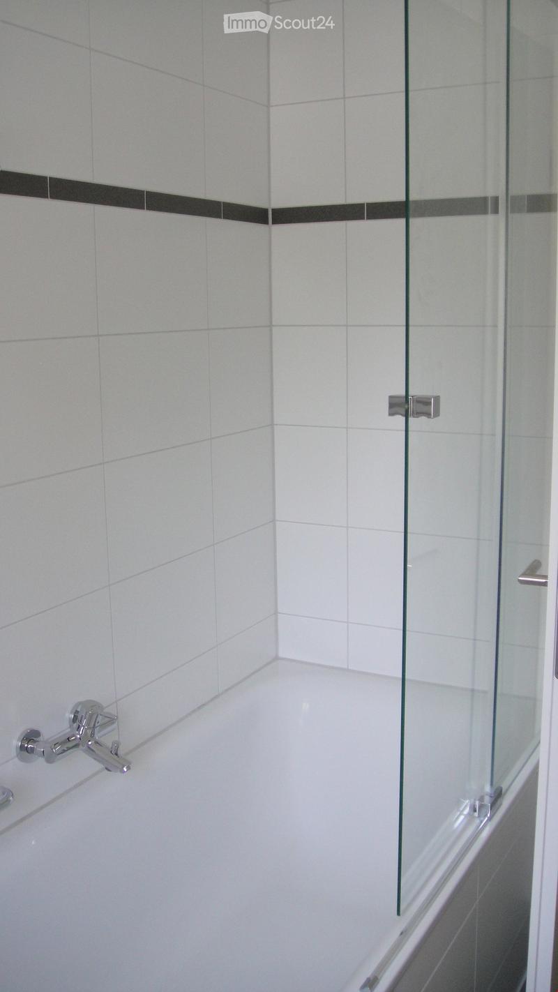 Modern bathroom with a white tiled bathtub, chrome faucet, and a glass shower enclosure with silver handles.