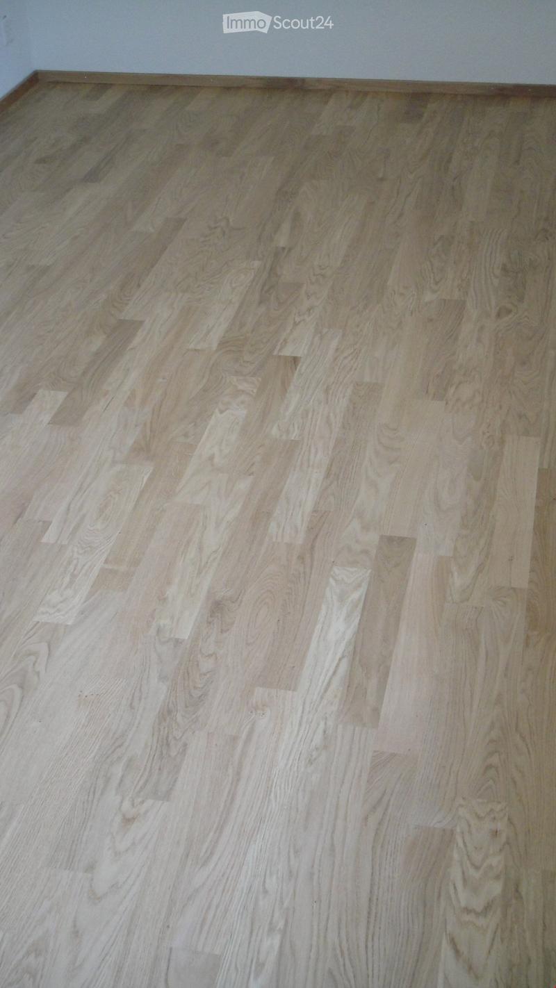 Empty room with light-colored wooden flooring and white walls.