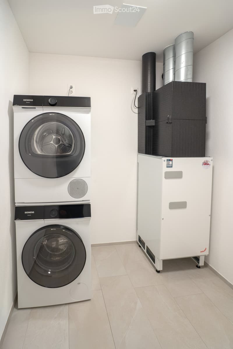 Modern bathroom with a white washing machine and dryer stacked vertically, along with a white water heater unit.