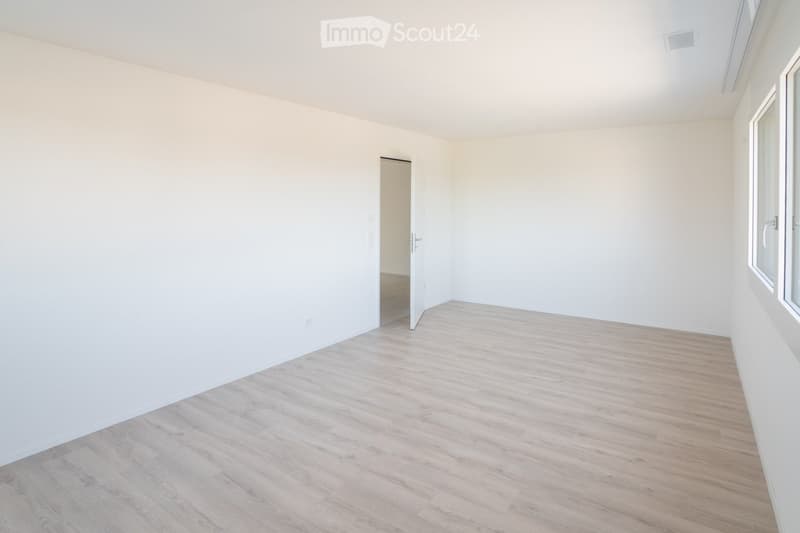 Empty room with white walls and light wooden flooring, featuring a single window and an open doorway leading to another space.