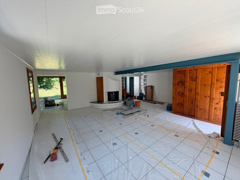 Empty room with white walls, tiled floor, and a fireplace area. Construction materials and tools are scattered around, indicating ongoing renovation.