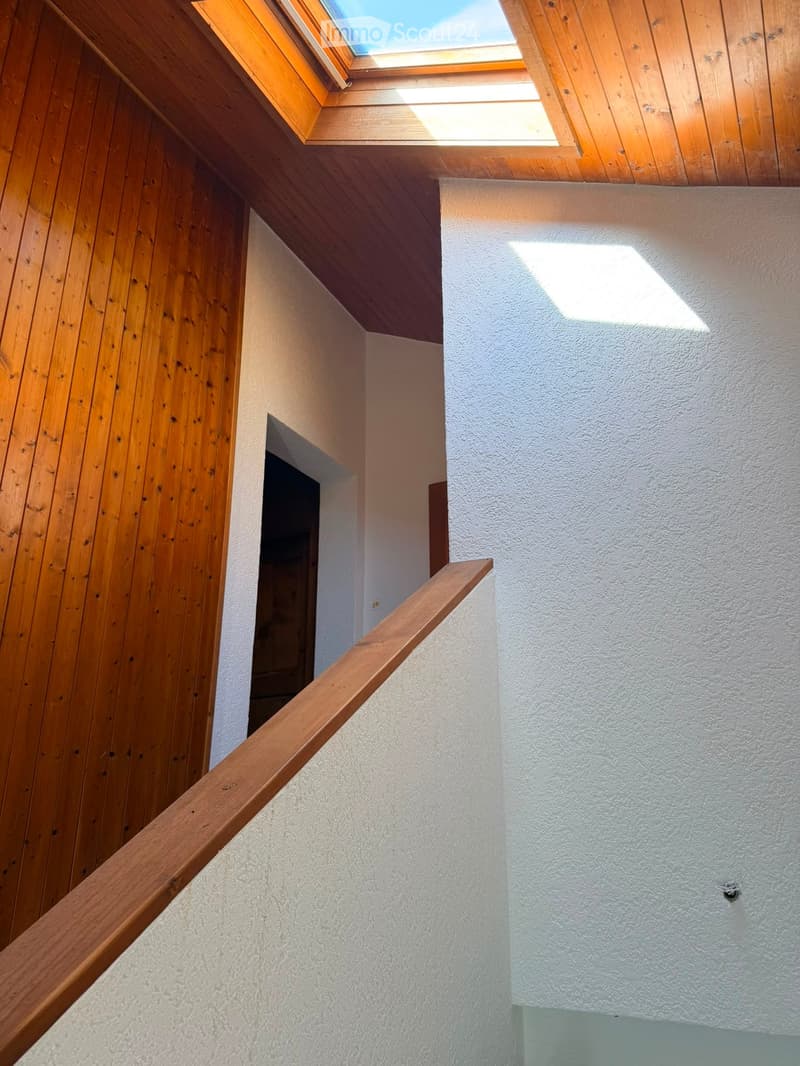 Wooden staircase with a slanted ceiling and skylight, white textured walls, and a wooden handrail.