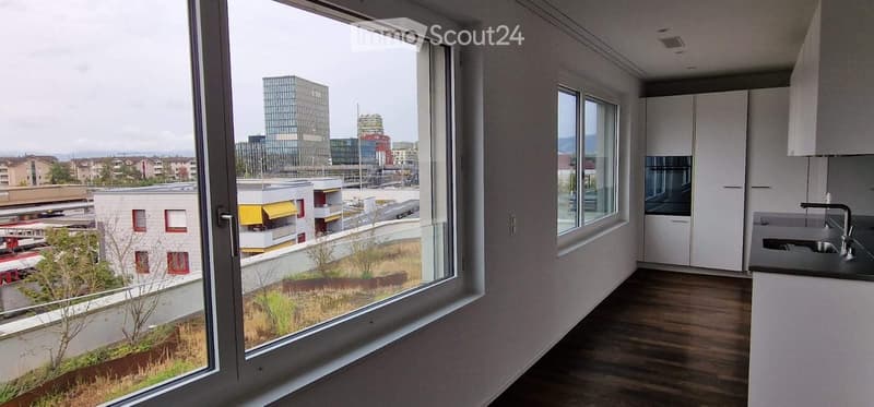 Modern kitchen with wooden flooring, large windows offering a city view, white cabinets, and a sink.