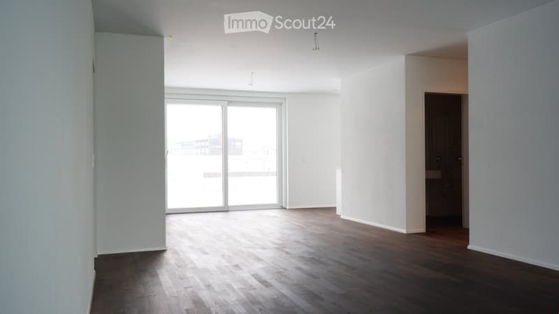 Empty room with wooden flooring, white walls, and a large sliding glass door leading to a balcony.