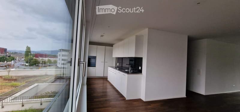 Modern kitchen with white cabinets, dark countertops, and a wooden floor, visible through large windows overlooking an outdoor area.