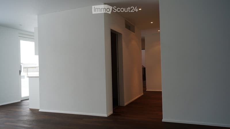 Empty hallway with wooden flooring, white walls, and a door leading to a balcony area.