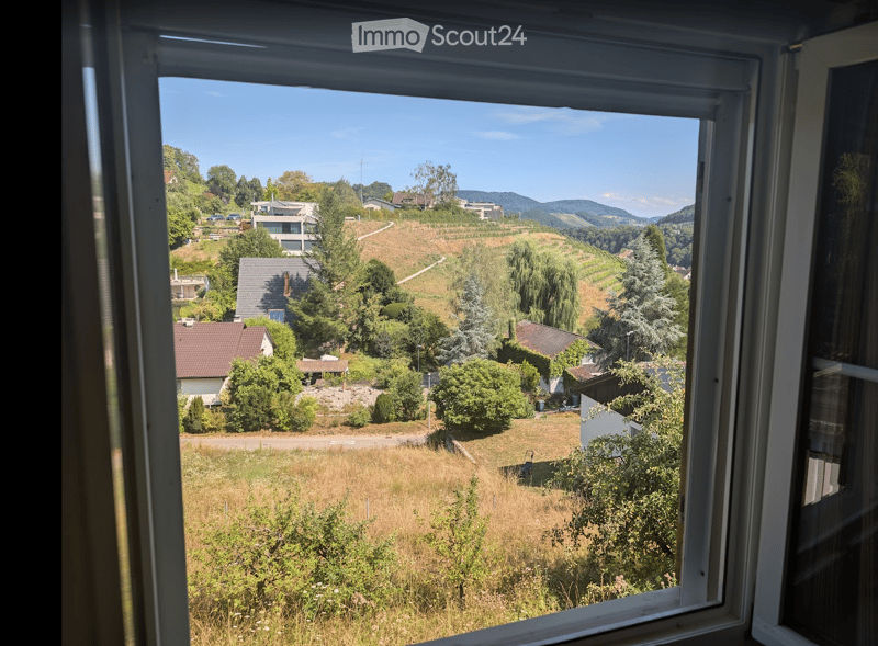 View from a window showing a scenic countryside with houses, trees, and rolling hills under a clear blue sky.