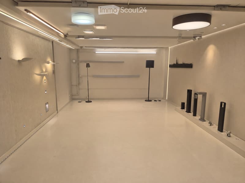 Modern hallway with white walls, recessed lighting, and a polished concrete floor. Minimalist decor includes a few floor lamps and wall-mounted lighting fixtures.
