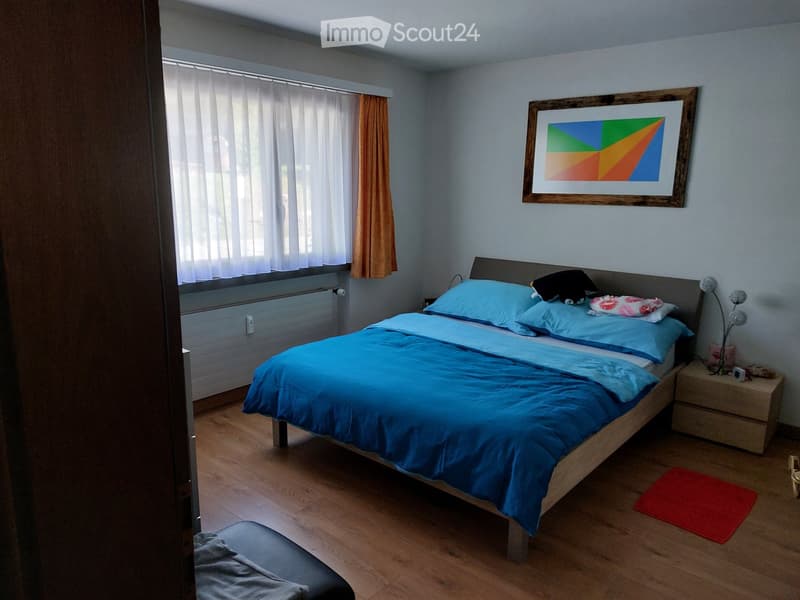 Cozy bedroom with a wooden bed, blue bedding, nightstand, picture frame, and a small red rug on the floor.