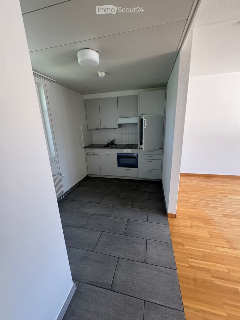 Modern kitchen with grey cabinets, stainless steel appliances, and grey tiled floor. The kitchen features a sink, faucet, oven, and refrigerator.