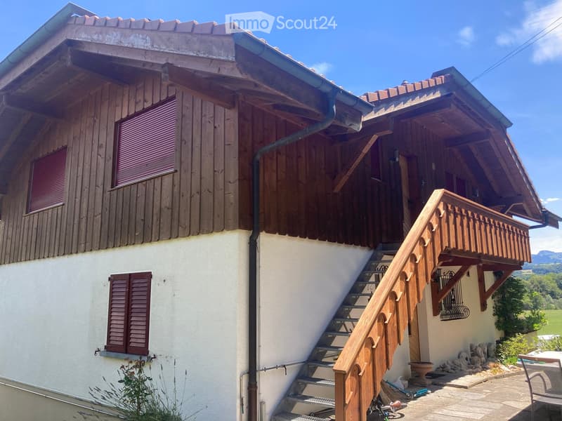 Two-story wooden house with a balcony, wooden shutters, and a staircase leading to the upper level.