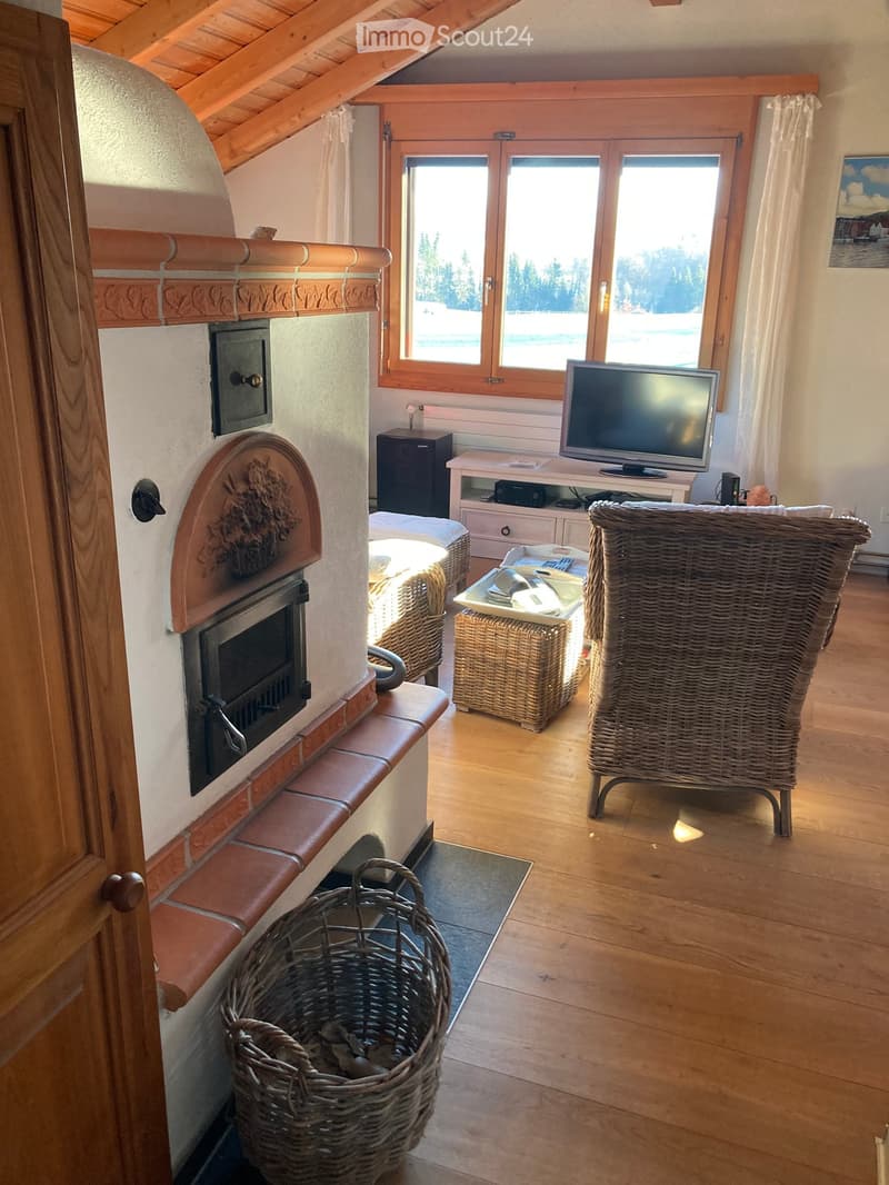 Cozy living room with wooden floors, fireplace, large windows offering a scenic view, wicker furniture, and a television.