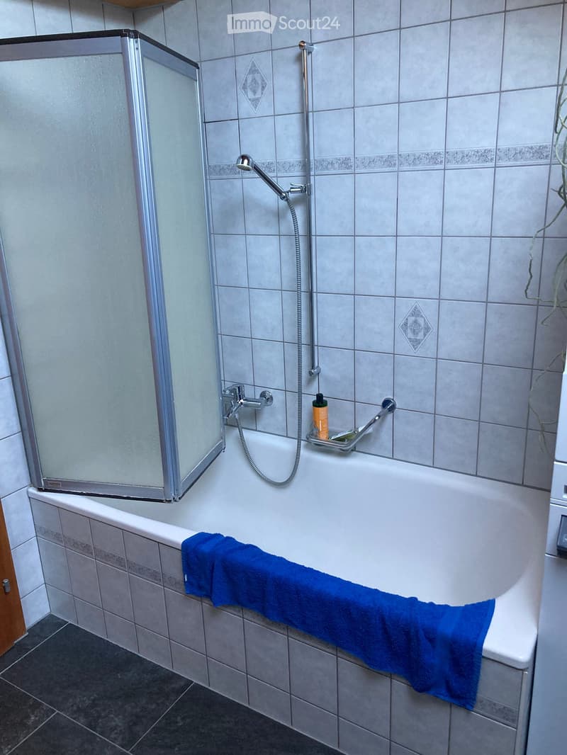 Modern bathroom with a bathtub, glass shower enclosure, and a blue towel draped over the edge of the tub.