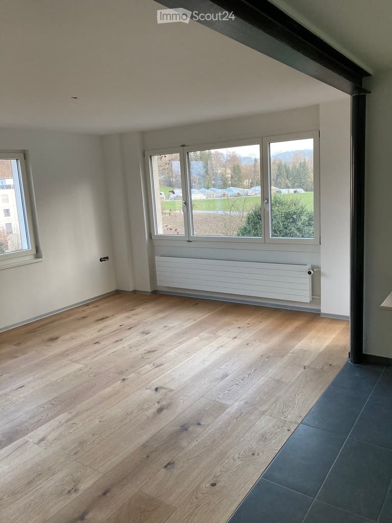 Empty room with wooden flooring, white walls, large windows, and a radiator. No furniture or equipment present.