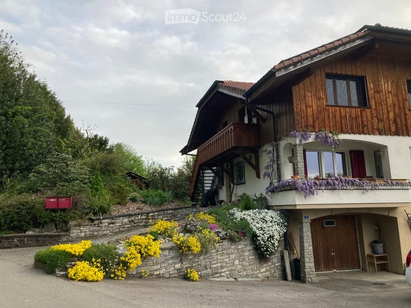 Two-story house with wooden balcony, stone walls, and colorful flowers in the garden.