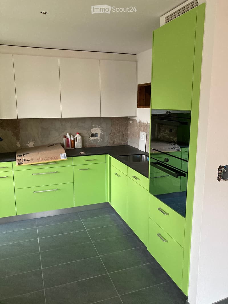 Modern kitchen with green and white cabinets, dark tiled floor, black countertop, and stainless steel sink and oven.
