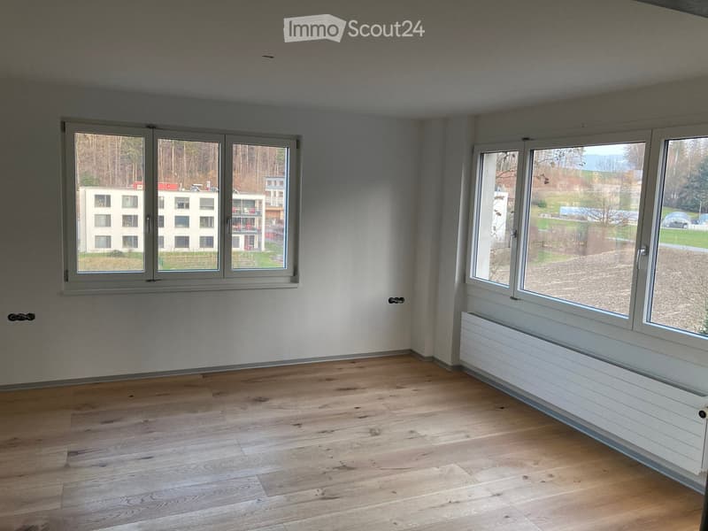 Empty room with wooden flooring, large windows, radiator, and white walls.