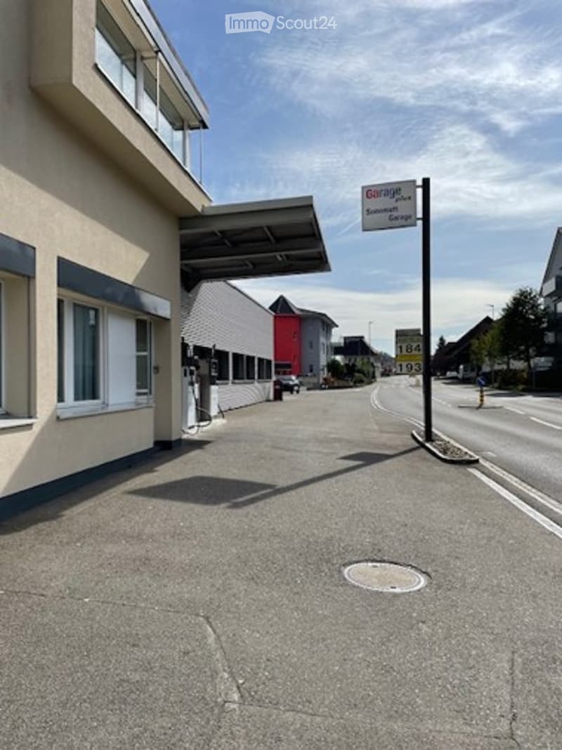 Modern building with a covered entrance and a sign indicating a garage service. The area includes a gas pump and a clear road leading to the building.