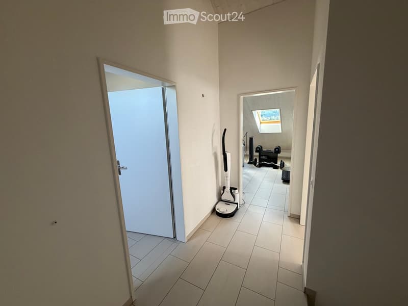 A clean, tiled hallway with white walls, featuring a robotic vacuum cleaner placed near the left wall and two open doors leading to other rooms.
