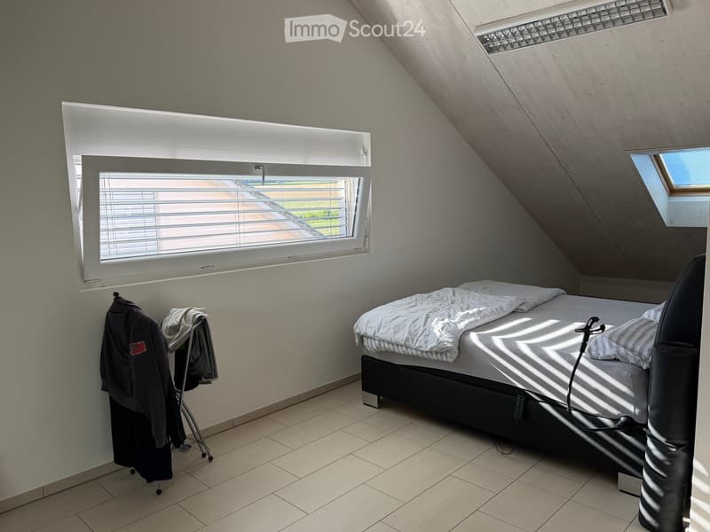 Bright attic bedroom with slanted ceilings, large windows, tiled floor, and a neatly made bed.