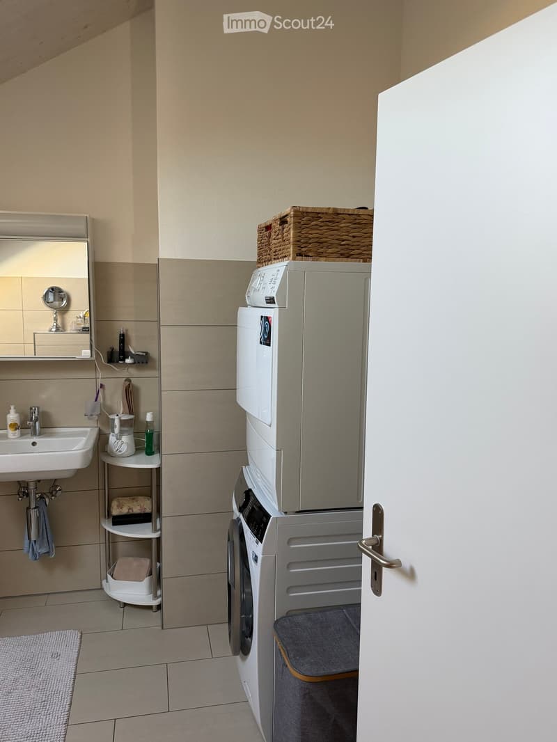 Bathroom with a sink, mirror, washing machine, refrigerator, wicker basket, and various toiletries.