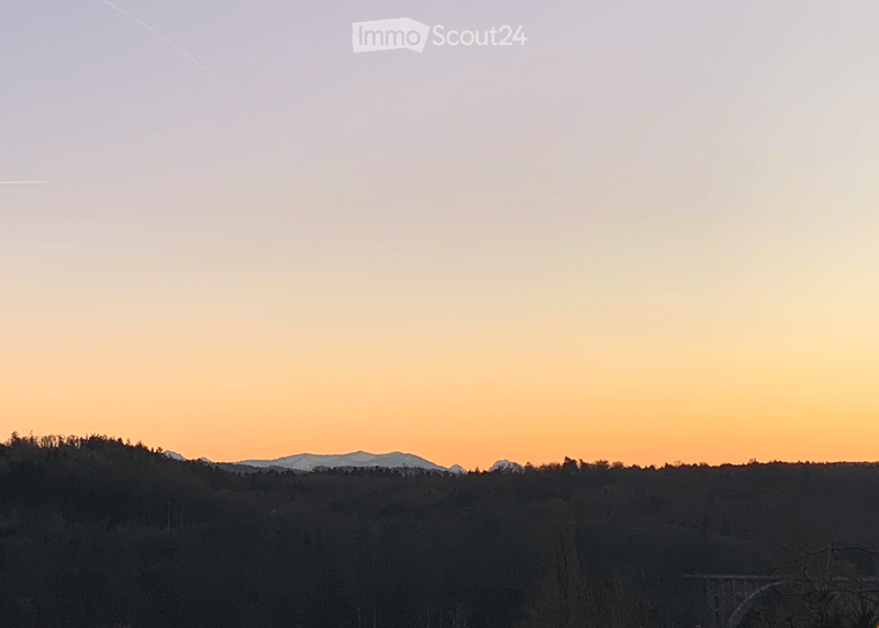 A serene view of a forested landscape at sunset, with mountains visible in the distance.