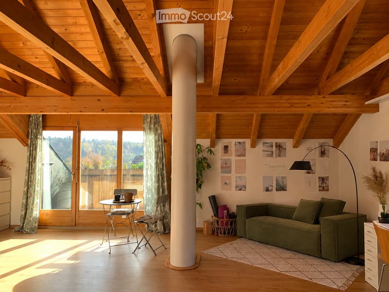 Bright living room with wooden beams, large windows, green sofa, small table, and artwork on the wall.