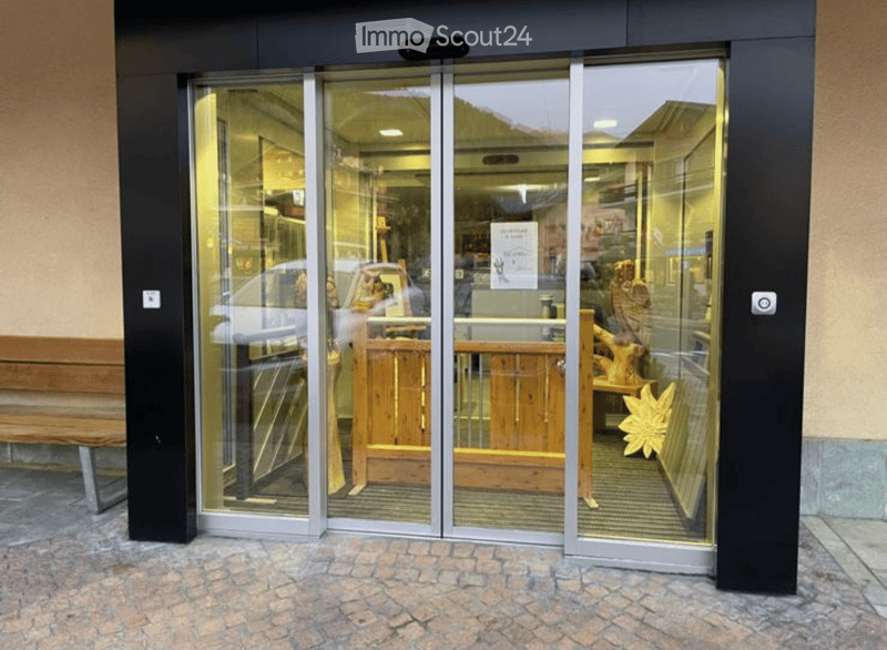 Entrance to a building with glass sliding doors, showing interior displays of wooden furniture and decorative items.