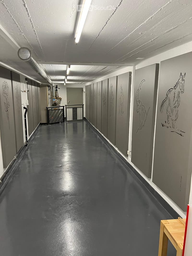Long, narrow hallway with dark, glossy flooring and white walls adorned with animal illustrations. Metal railing and industrial equipment visible.