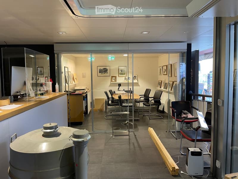 Office space with glass partitions, a reception area, meeting table, chairs, and framed artwork on the walls.