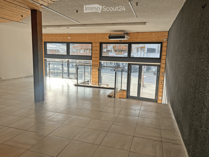 Empty hallway with tiled floor, wooden paneling, large windows, and a glass door leading to an outdoor area.