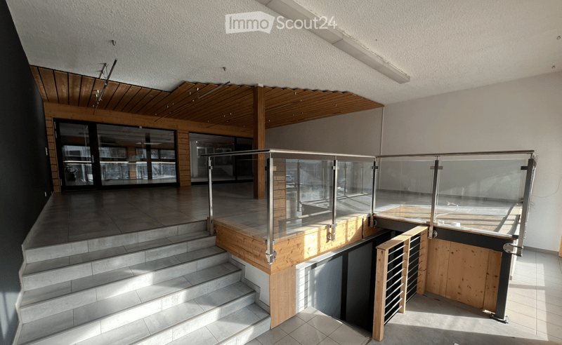 Modern hallway with wooden ceiling, glass railing, and steps leading to a lower level.