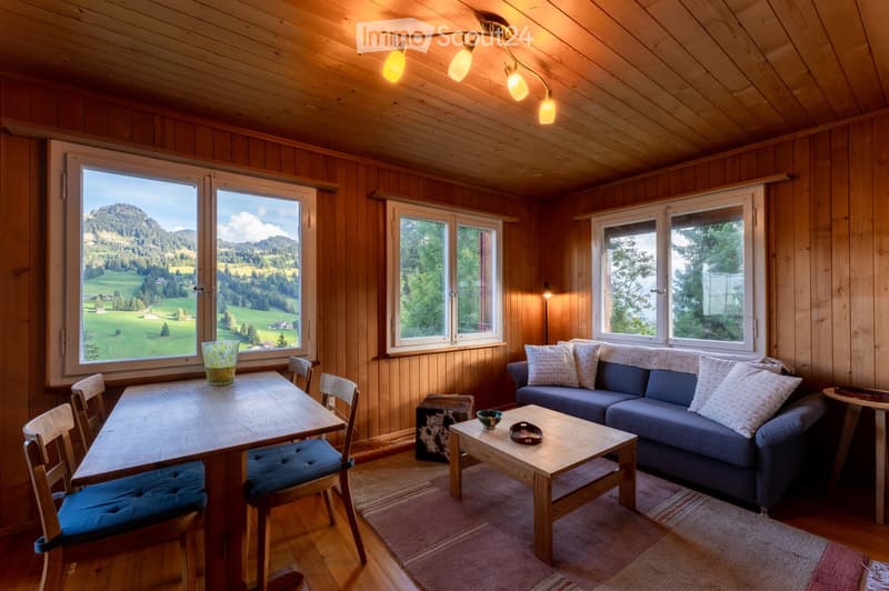 A cozy room with wooden interior and large windows, sofa, coffee table, dining table with chairs, carpet, a bowl, decorative items, and a scenic view outside.